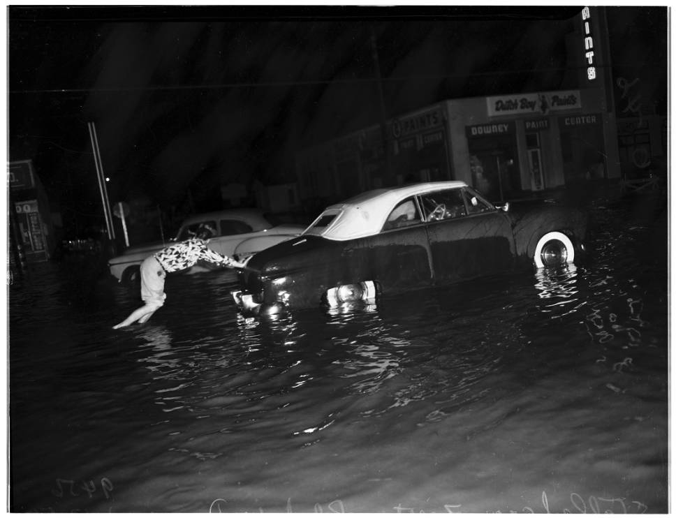 Despite channelization, flooding still occurred during heavy rains as seen here with a woman pushing her car through high water, 1952